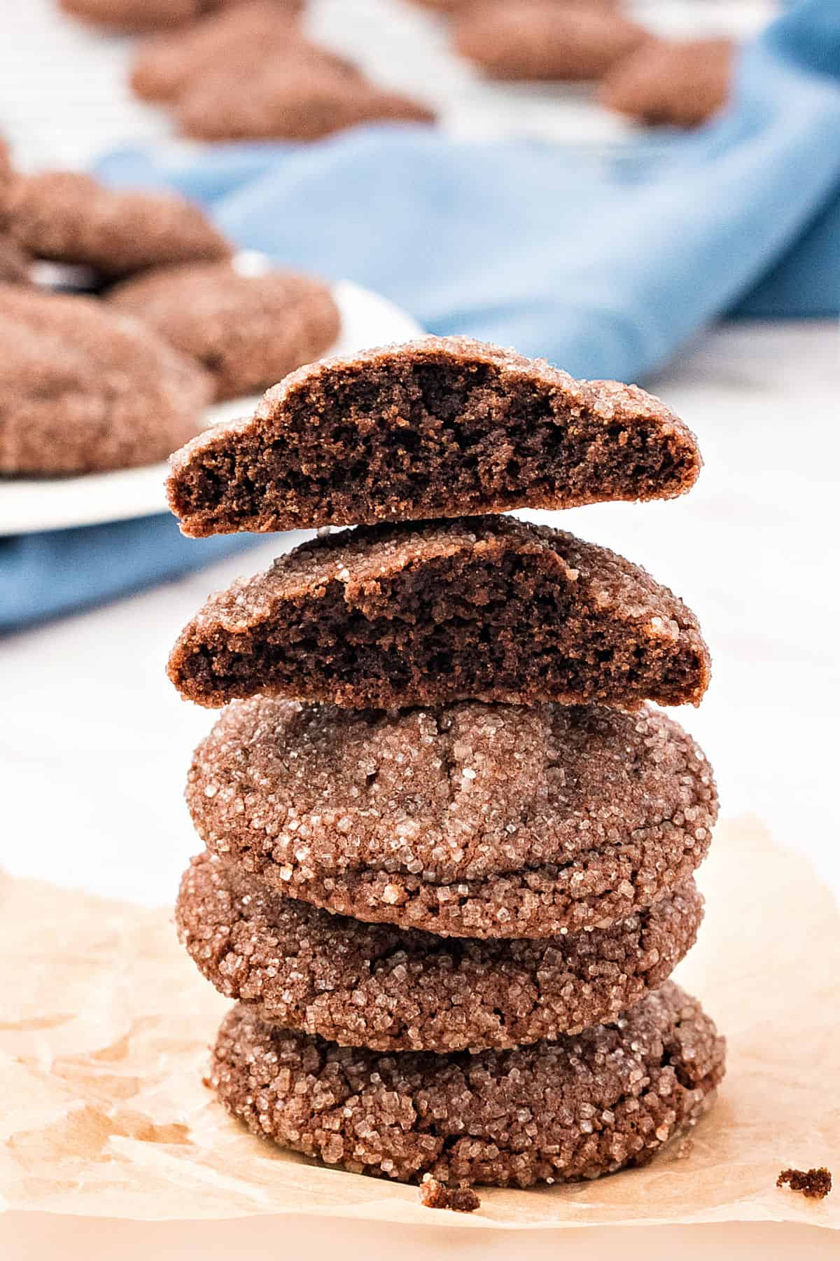 Two half chocolate cookies on a stack of whole ones. Beige and blue background.