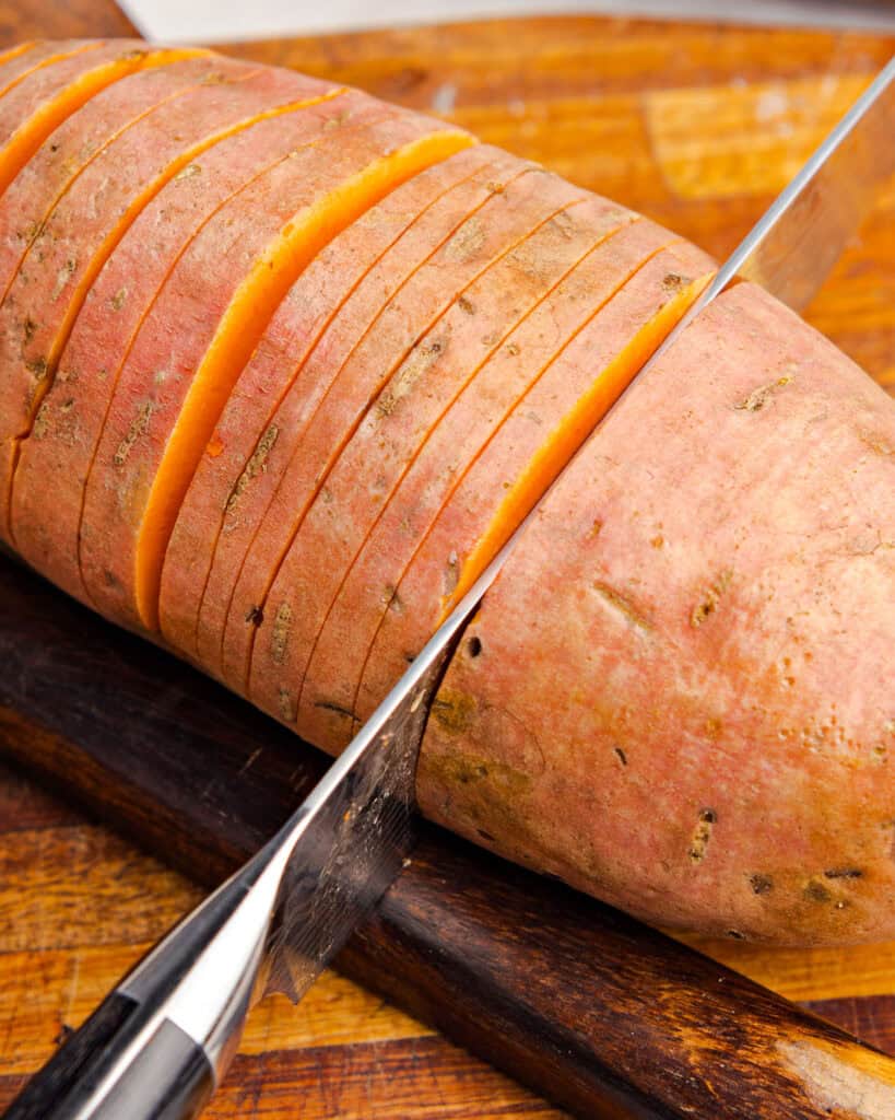 Slicing unpeeled sweet potato on a wooden board.