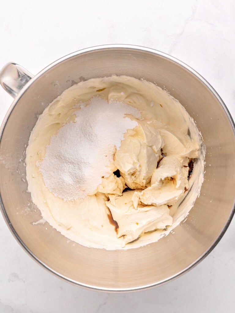 Mixing mascarpone filling ingredients in a metal bowl. White background.
