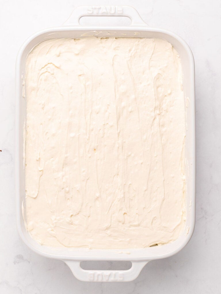 Final mascarpone layer for tiramisu in a white ceramic dish.