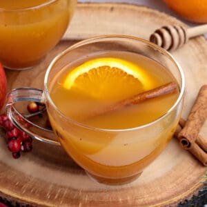Wooden board with glass cups of apple drink with orange slice and cinnamon stick.