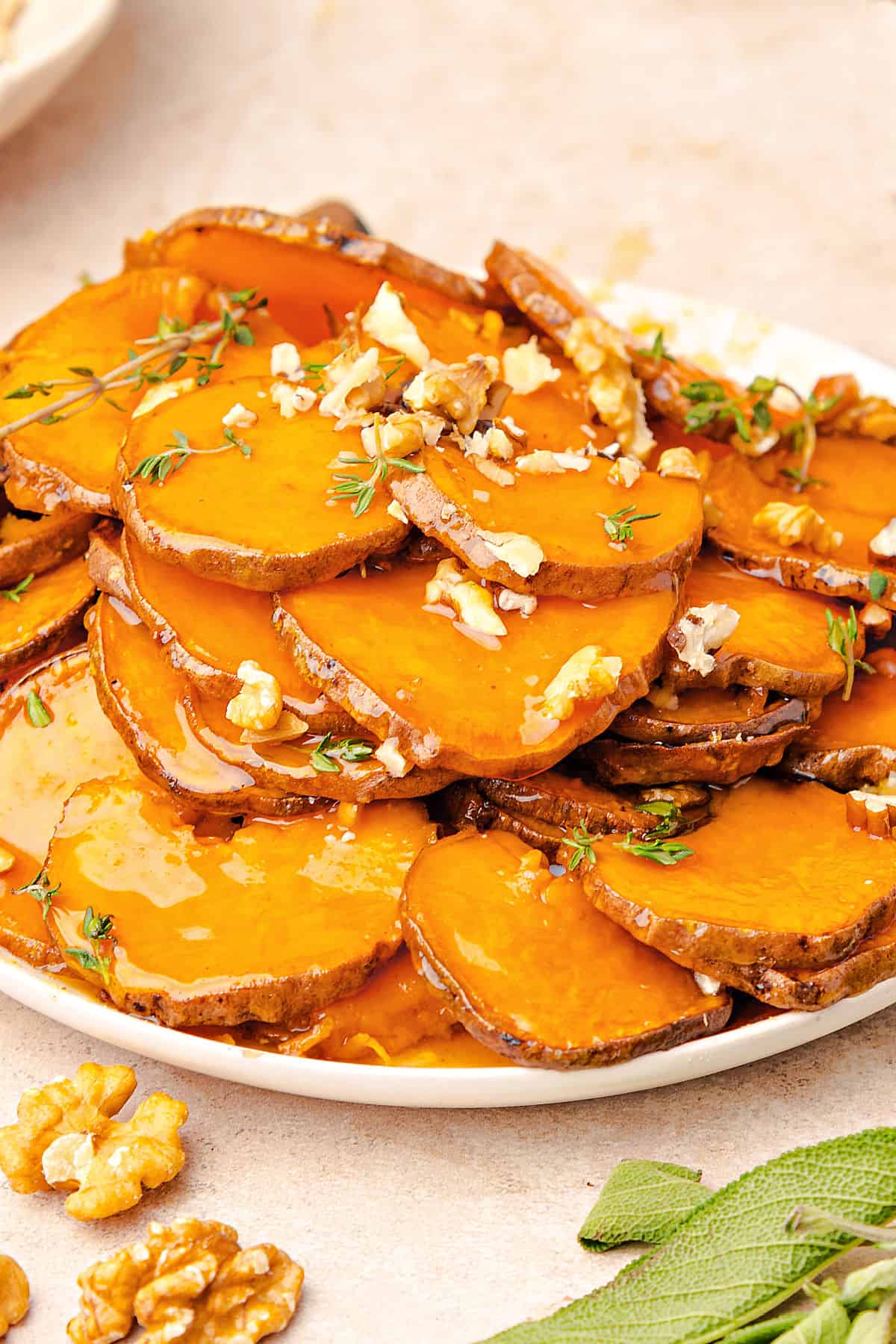Pile of honey sweet potato slices on a white plate. Pinkish background. Chopped walnuts.