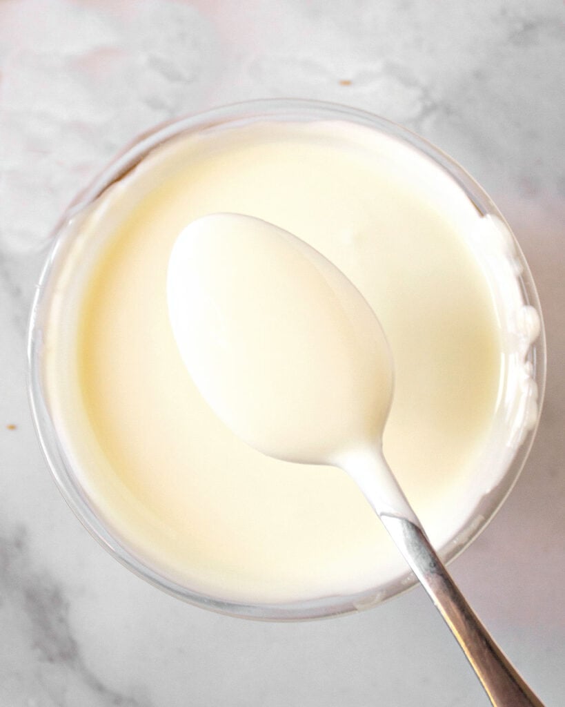 Melted white chocolate being spooned from glass bowl. Marbled background.