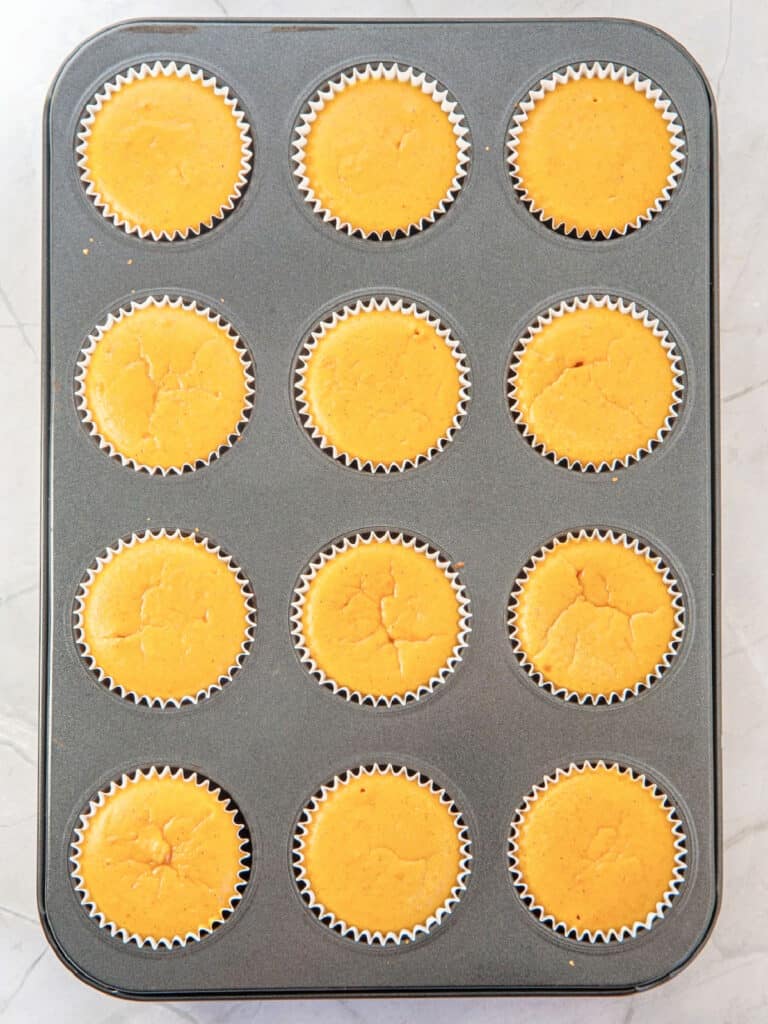 Metal muffin pan with baked mini pumpkin cheesecakes.