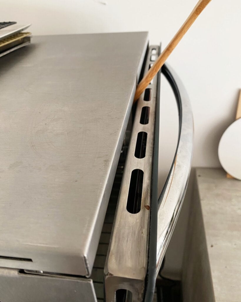 Metal oven with wooden spoon keeping the door ajar.