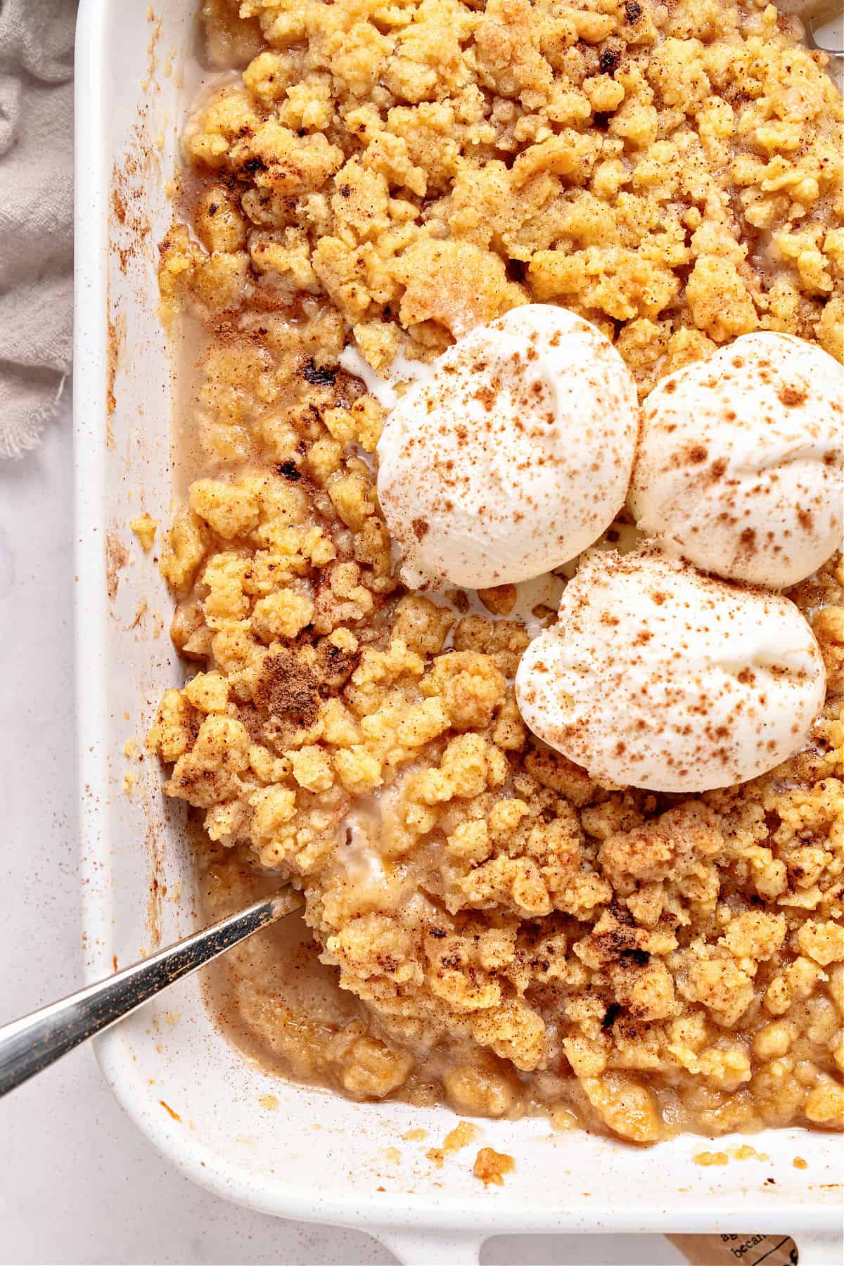 Partial view of white dish with pear crumble topped with whipped cream.