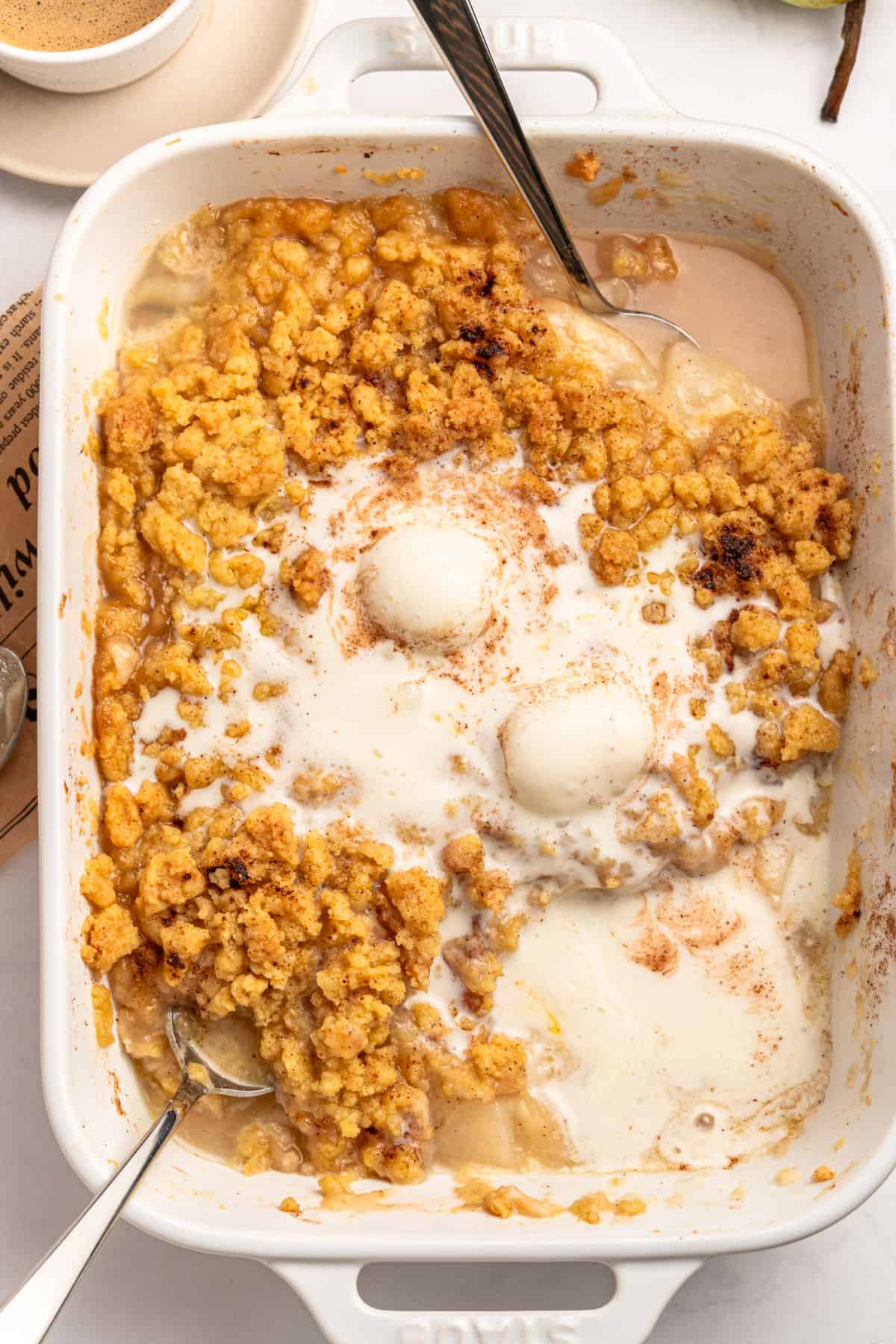 Ice cream topped pear crumble in white rectandular dish. Silver spoons.