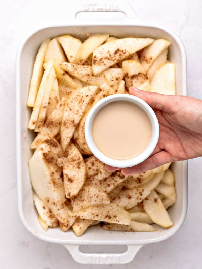 Cornstarch slurry in white bowl held over white dish with spiced pear sliced.