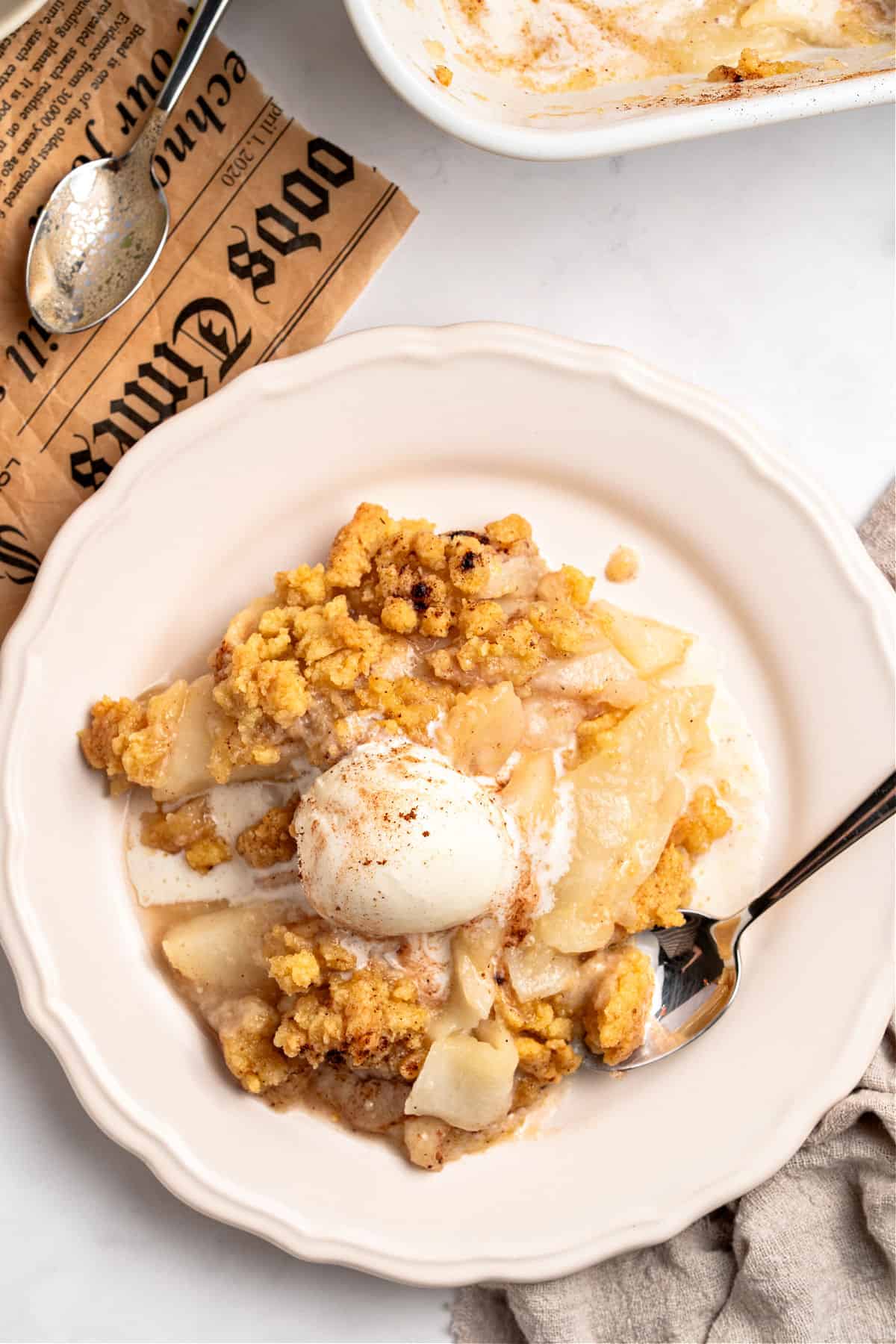 White plate with pear crumble and cream serving. Silver spoon.