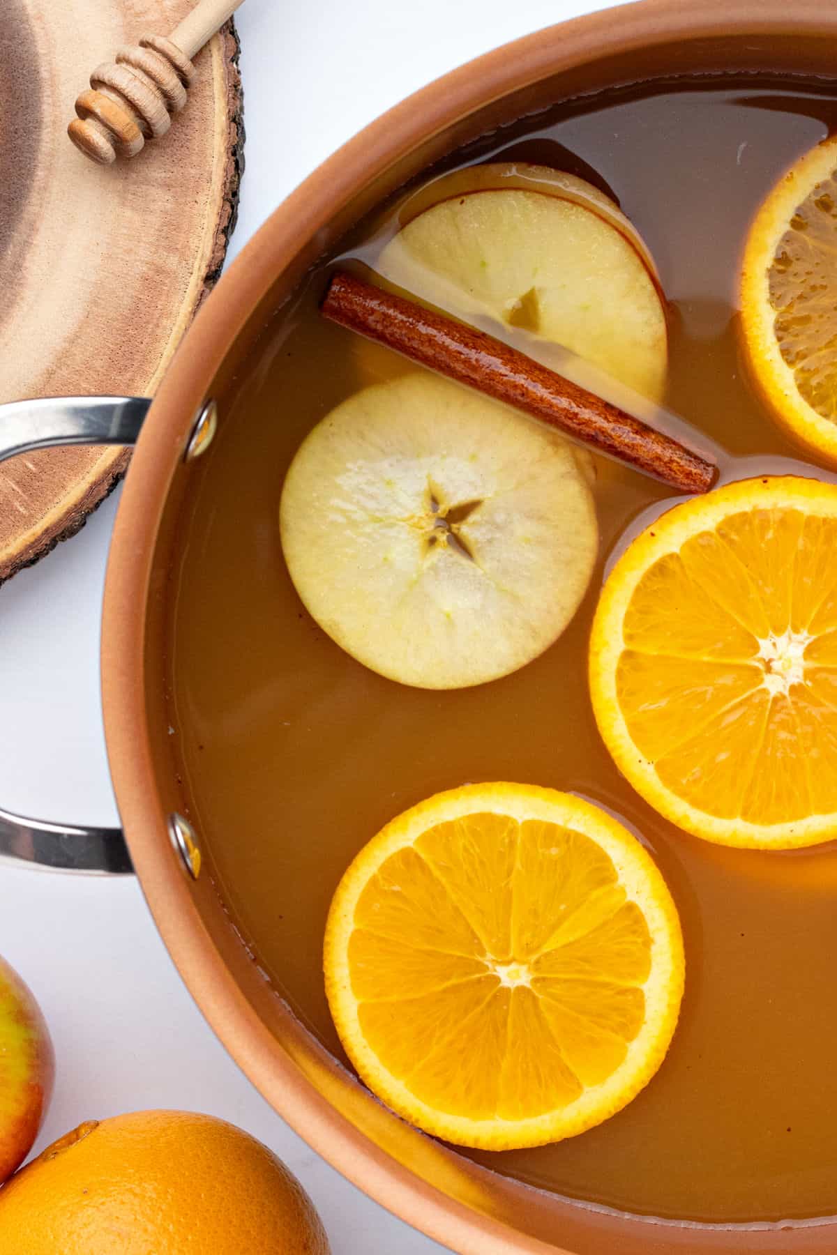 Partial view of copper pot with apple cider mix, orange and apple rounds and cinnamon stick.