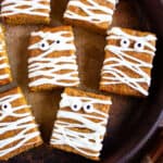 Several mummy pumpkin blondies with candy eyes. Dark brown background.