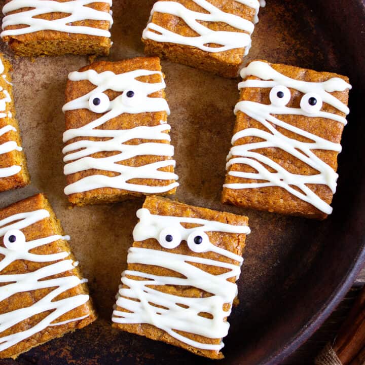 Several mummy pumpkin blondies with candy eyes. Dark brown background.