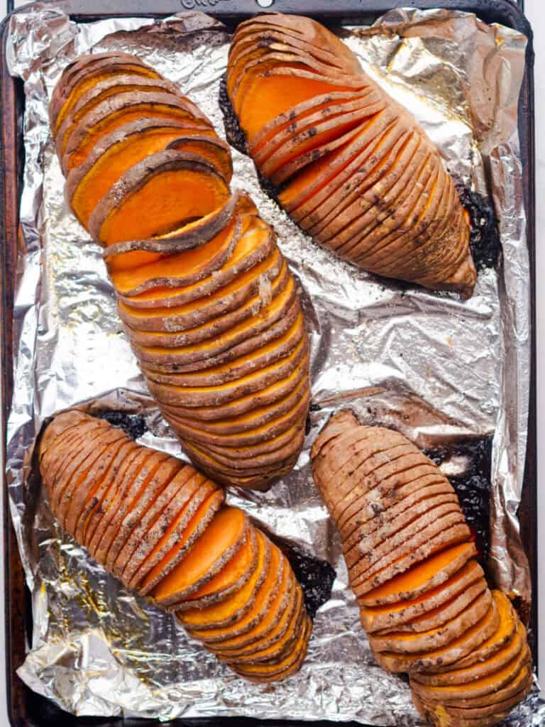 Foil-lined baking sheet with baked hasselback sweet potatoes.