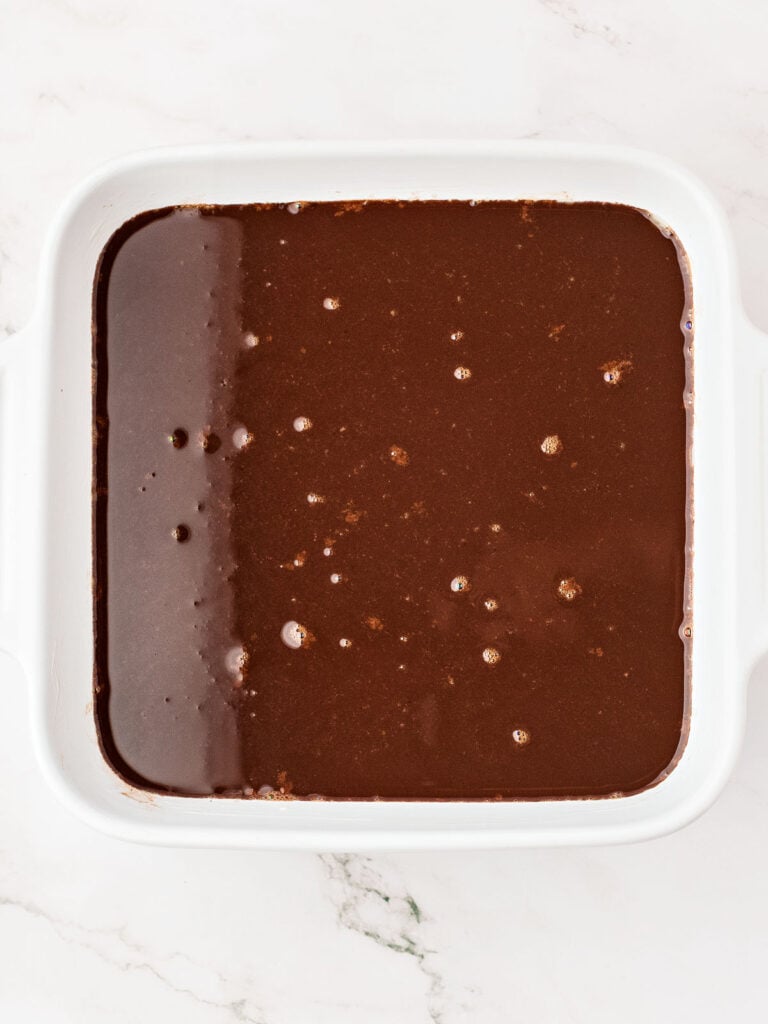 Custard-topped brownie cake in a white square dish. White marbled surface.