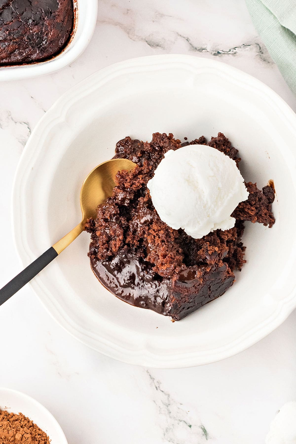 White bowl with hot fudge pudding cake and scoop of ice cream. White marble background.