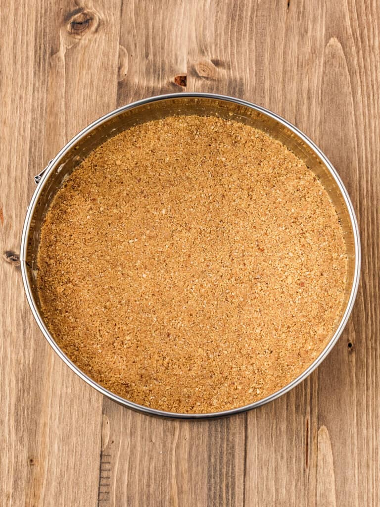 Round metal pan with cheesecake graham crust. Wooden background.