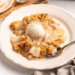 Close up of white plate with pear crumble and cream serving. Silver spoon.