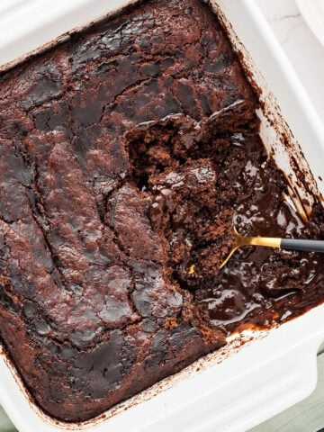 Close up white square dish with brownie pudding cake. Spoon inside.