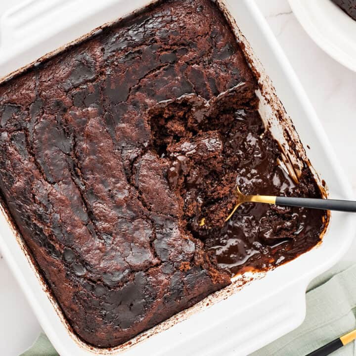Close up white square dish with brownie pudding cake. Spoon inside.