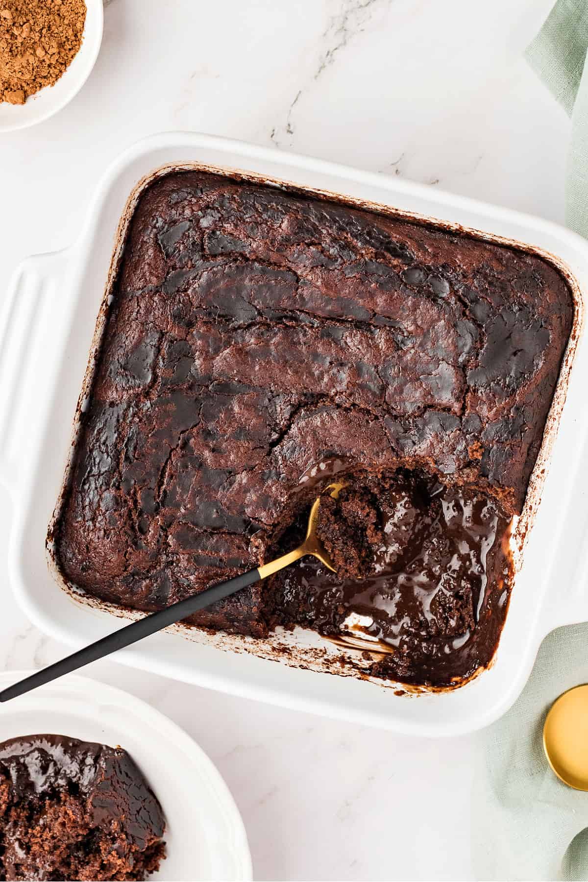 White square ceramic dish with chocolate pudding cake. Spoon inside. Marbled background. 
