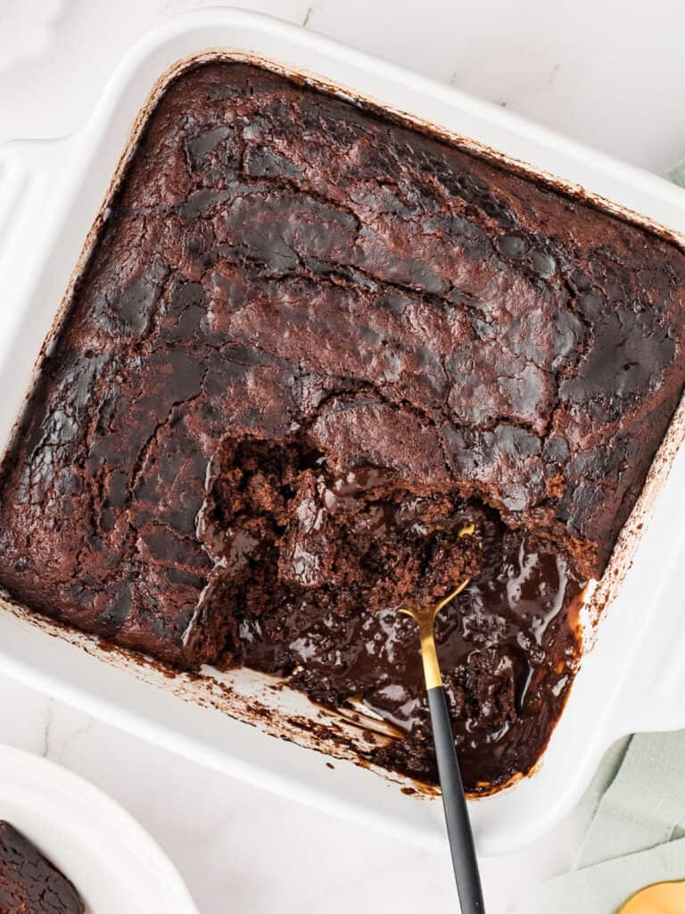Spoon inside a white baking dish with chocolate fudge pudding cake.