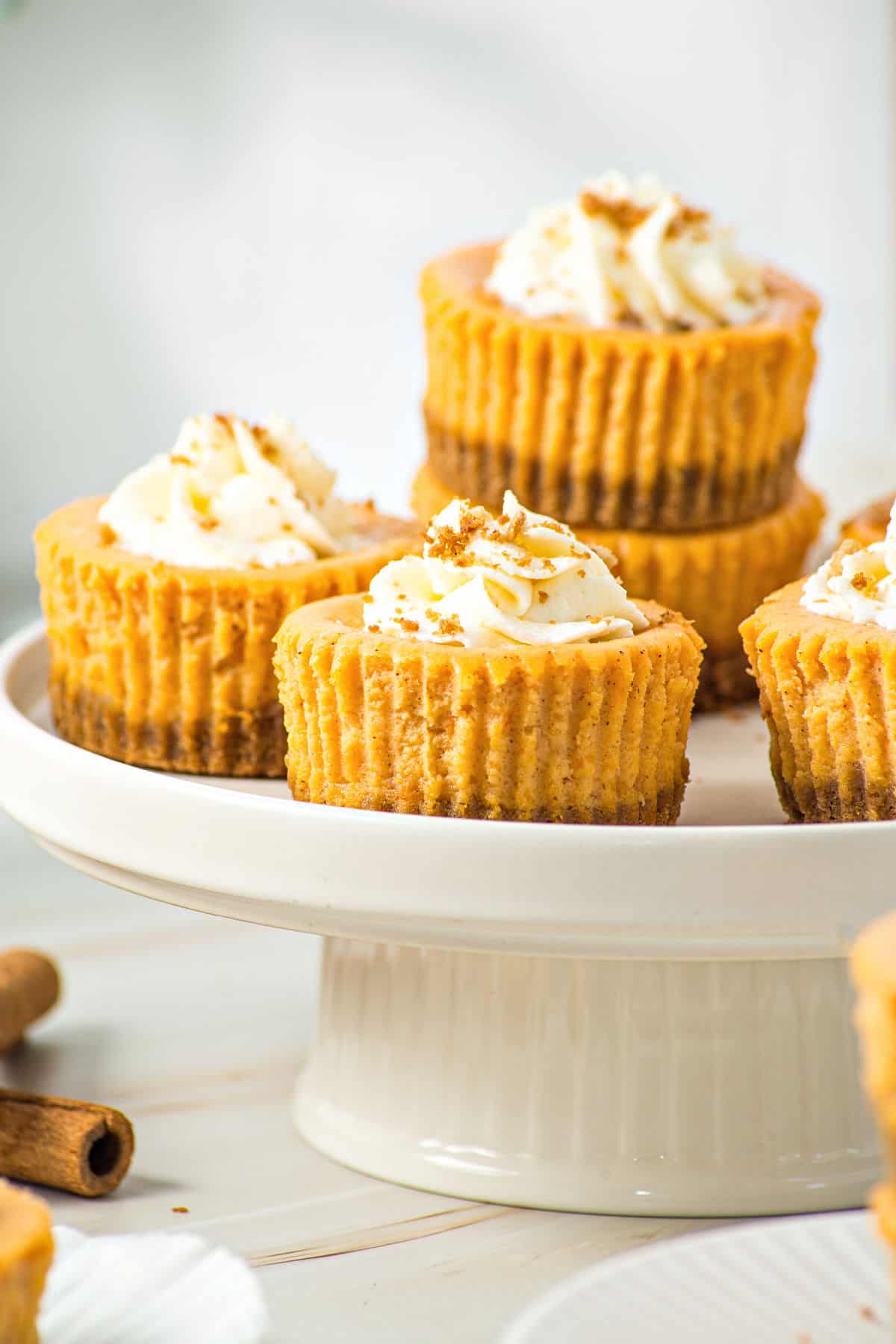 Several mini pumpkin cheesecakes on a white cake stand . Gray background.