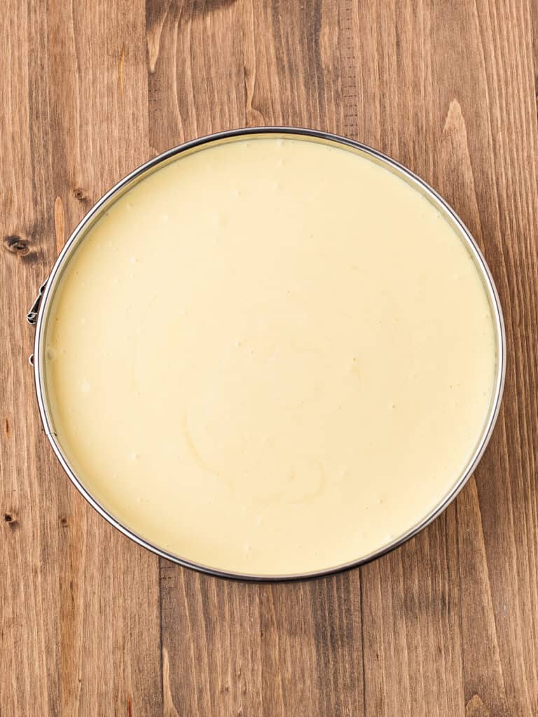 Cheesecake batter in a metal round pan on a wooden surface.