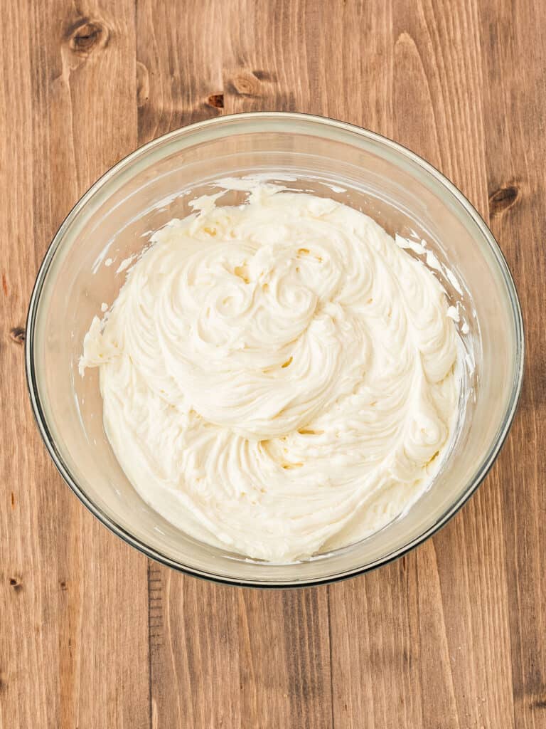 Glass bowl with cream cheese sugar mixture for cheesecake. Wooden background.