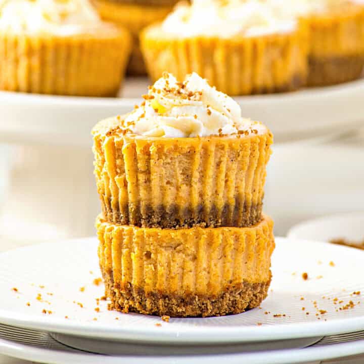 Stacked individual pumpkin cheesecakes with whipped cream. White plate.