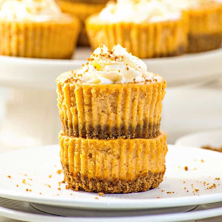 Stacked individual pumpkin cheesecakes with whipped cream. White plate.