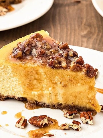Maple pecan topped cheesecake slice on a white plate. Wooden background.