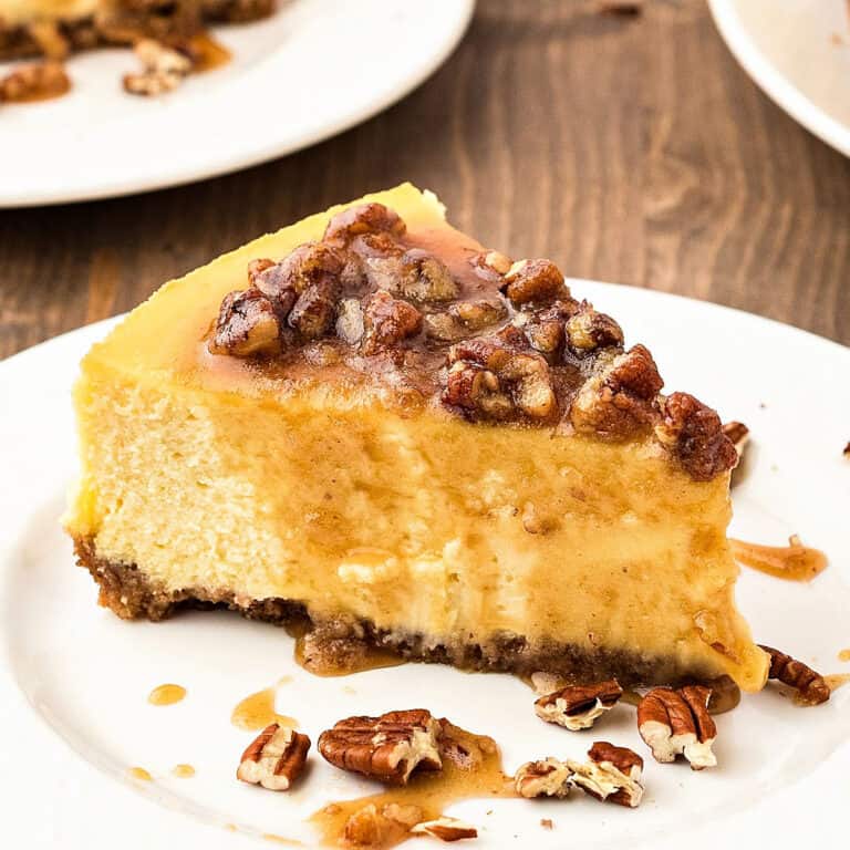 Maple pecan topped cheesecake slice on a white plate. Wooden background.