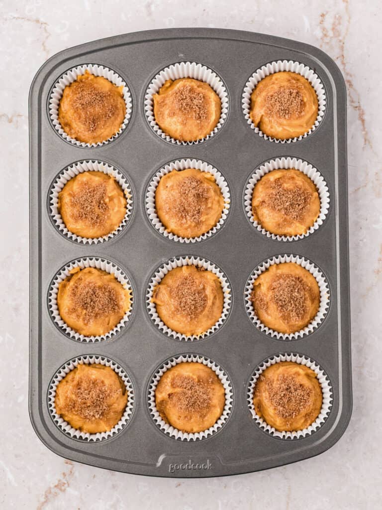 Sugar-topped sweet potato muffins batter in paper liner. Dark muffin pan.