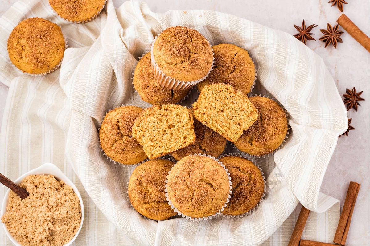 One halved muffin atop several whole in a cheesecloth-lined basket.