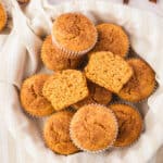 Kitchen towel lined basket with pile of sweet potato muffins. One is halved.