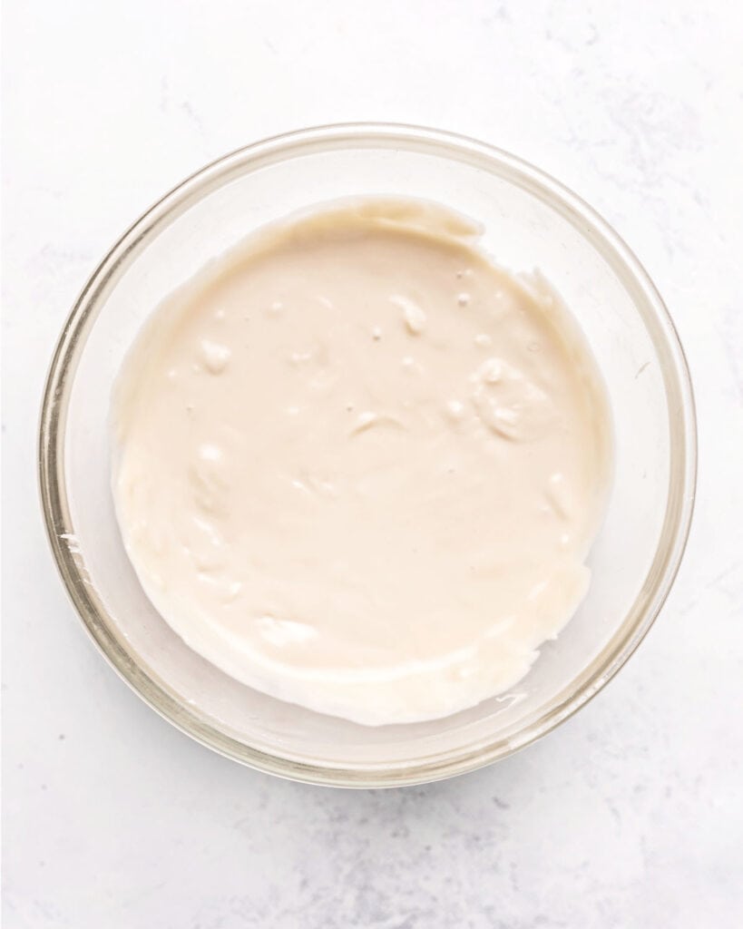 Melted white chocolate in a glass bowl. White background.