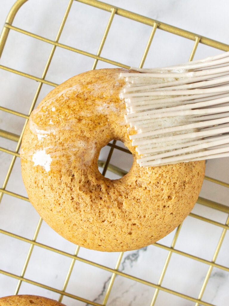 Brushing baked donut with melted butter on a wire rack.