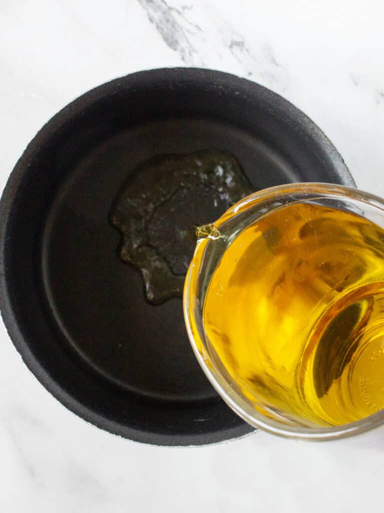 Pouring apple cider into a black saucepan. White marbled background.