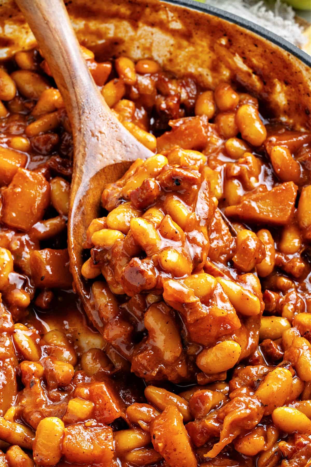 Close up wooden spoon with baked beans and apples in the pot.