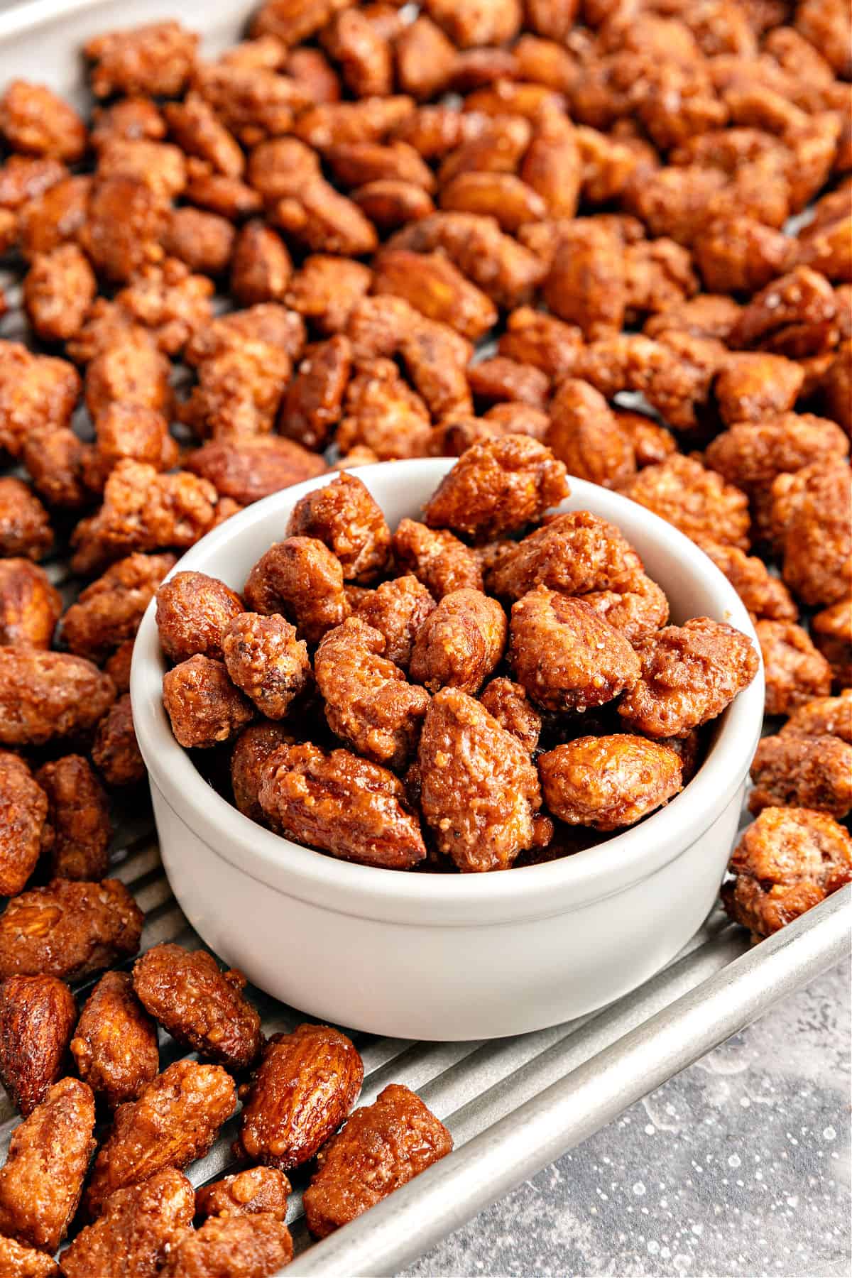 Pile of candied almonds in a white bowl and baking sheet.
