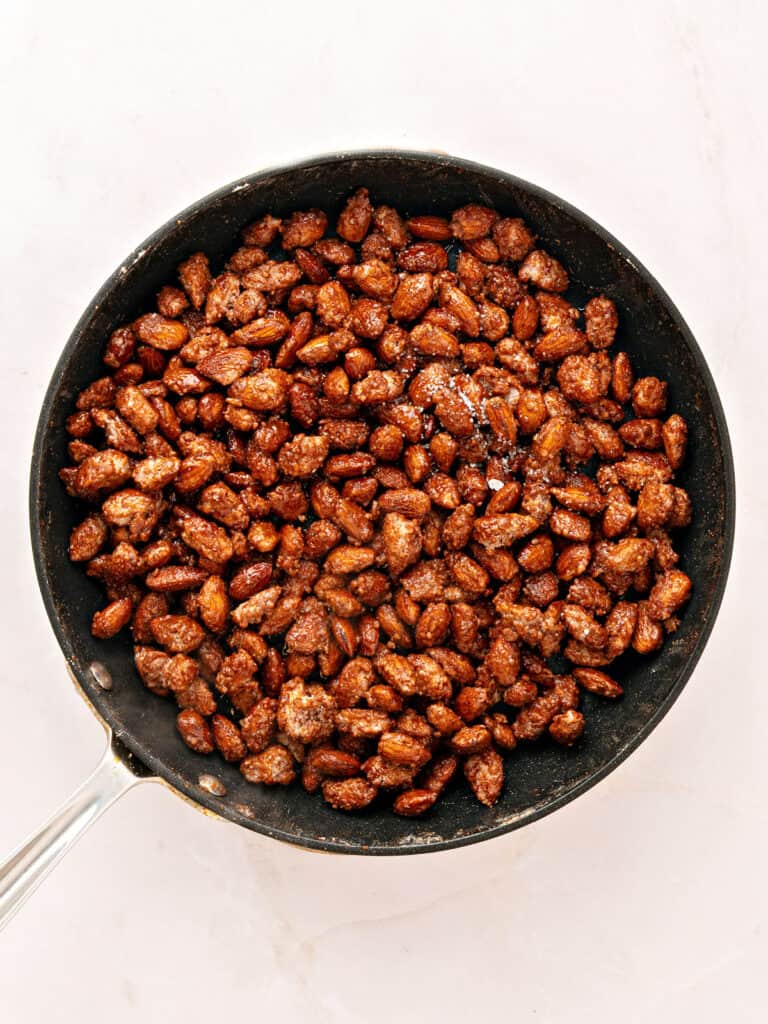 Sugar coated almonds in a black skillet. Light-colored background.