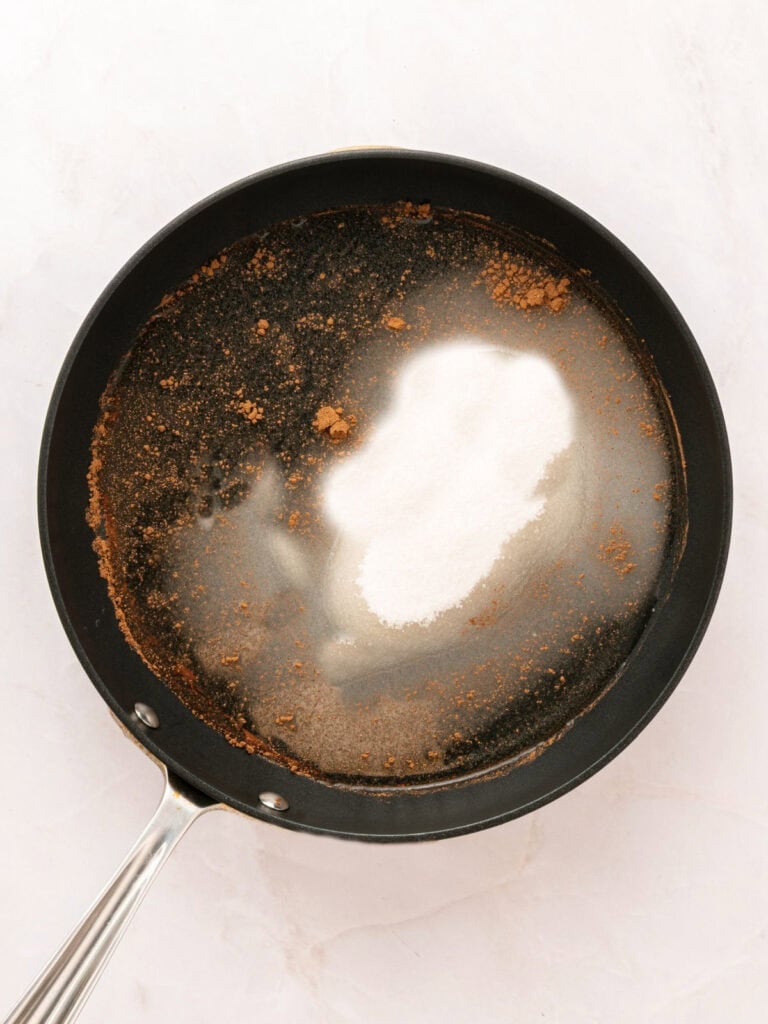 Black skillet with sugar, water and brown sugar. Light-colored surface.
