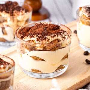 Individual tiramisu glass cups on a wooden board.