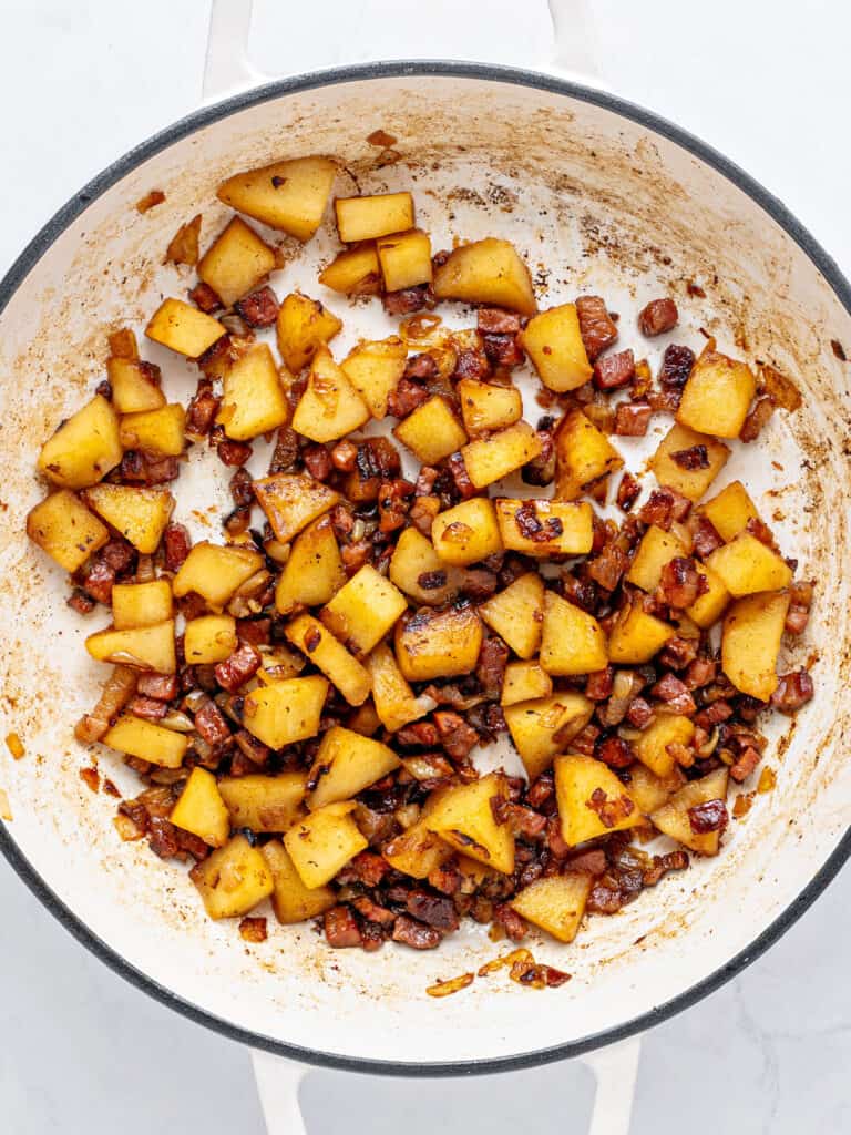 Diced apples, bacon and onion in a white pot with black rim.