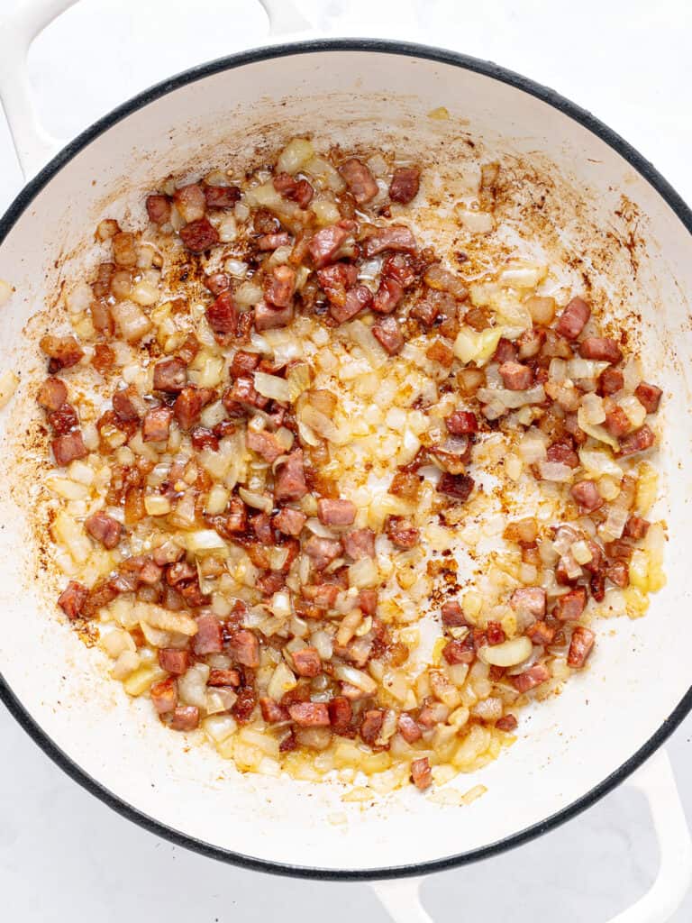 Onion and bacon cooking in a black-rimmed white pot.