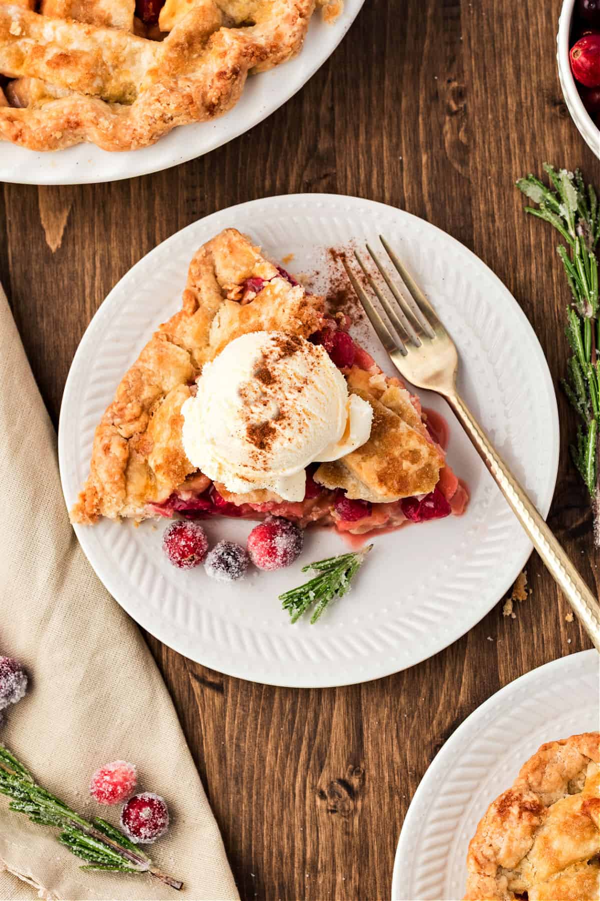 White plate with apple cranberry lattice pie slice with ice cream. Dark wood background.