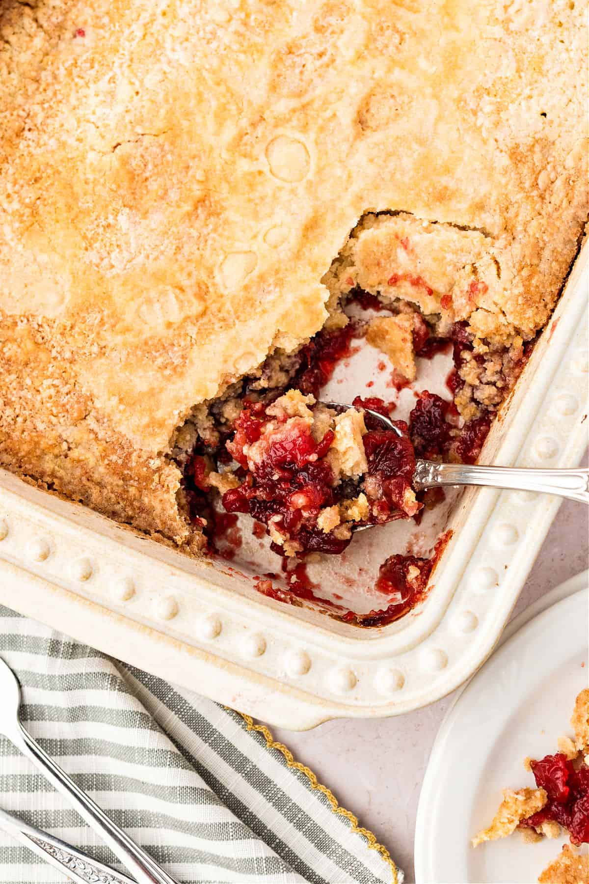 Cream-colored dish with cranberry dump cake. Serving missing. Close up.