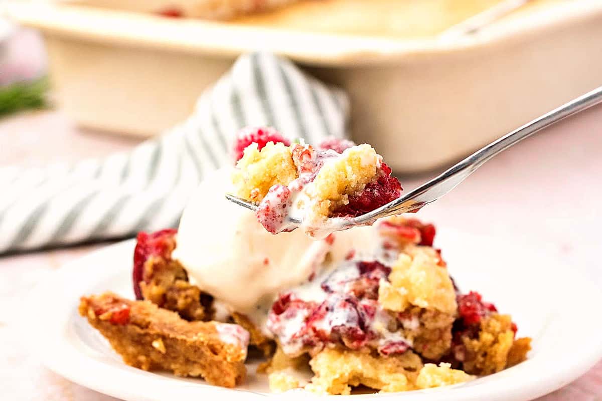 Bite of cran dump cake serving and ice cream. Cream colored background, green striped cloth.