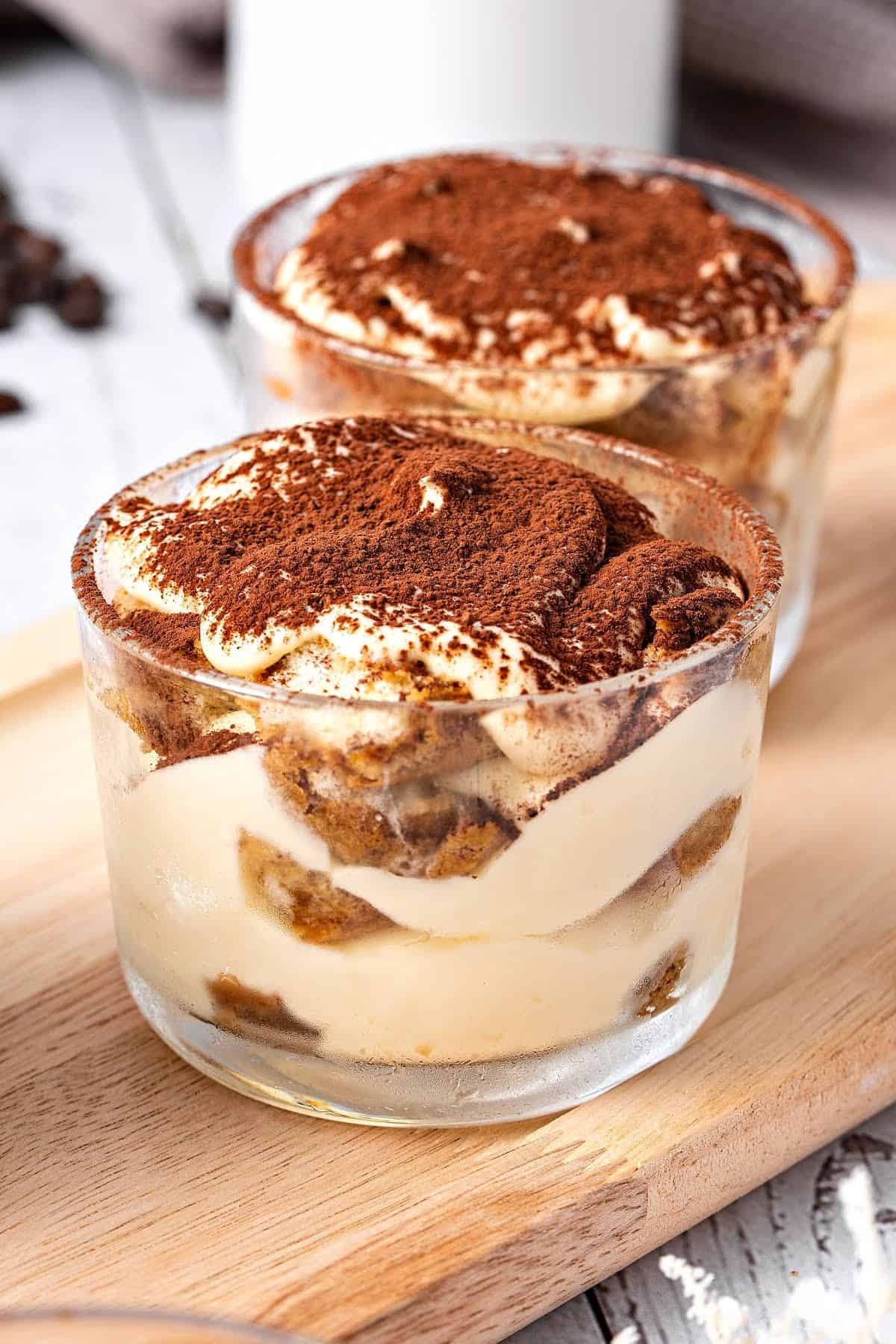 Two glasses with servings of classic tiramisu on a wooden board.
