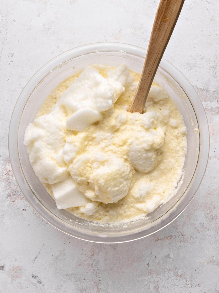 Beaten egg whites with ricotta filling in a glass bowl. Wooden spatula. Light gray background.